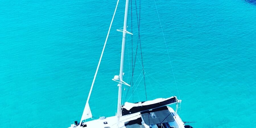 Catamarano Mysailcruise in navigazione nelle acque cristalline di Panarea, Isole Eolie, con isolotti e paesaggio mediterraneo al tramonto.