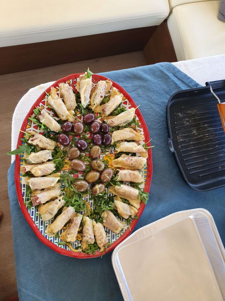 Deliziosi involtini di pesce spada alla siciliana, preparati freschi e serviti a bordo di una barca a vela durante una crociera gastronomica.