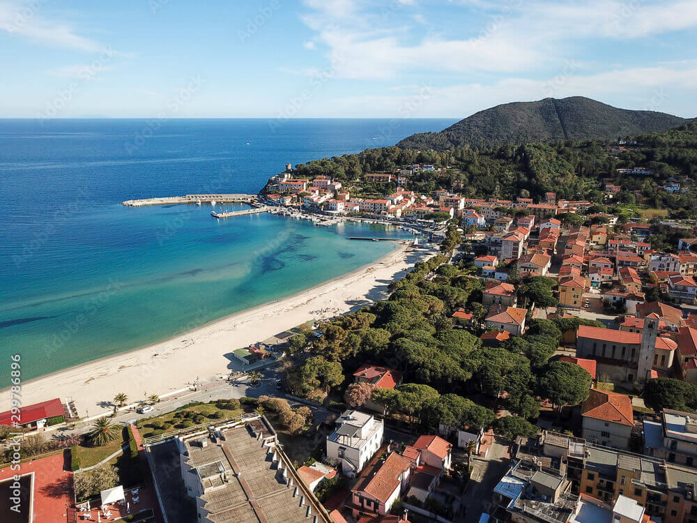 Ampia spiaggia di sabbia chiara a Marina di Campo, Isola d'Elba, con vista sul paese e catamarani ancorati per una crociera di lusso.