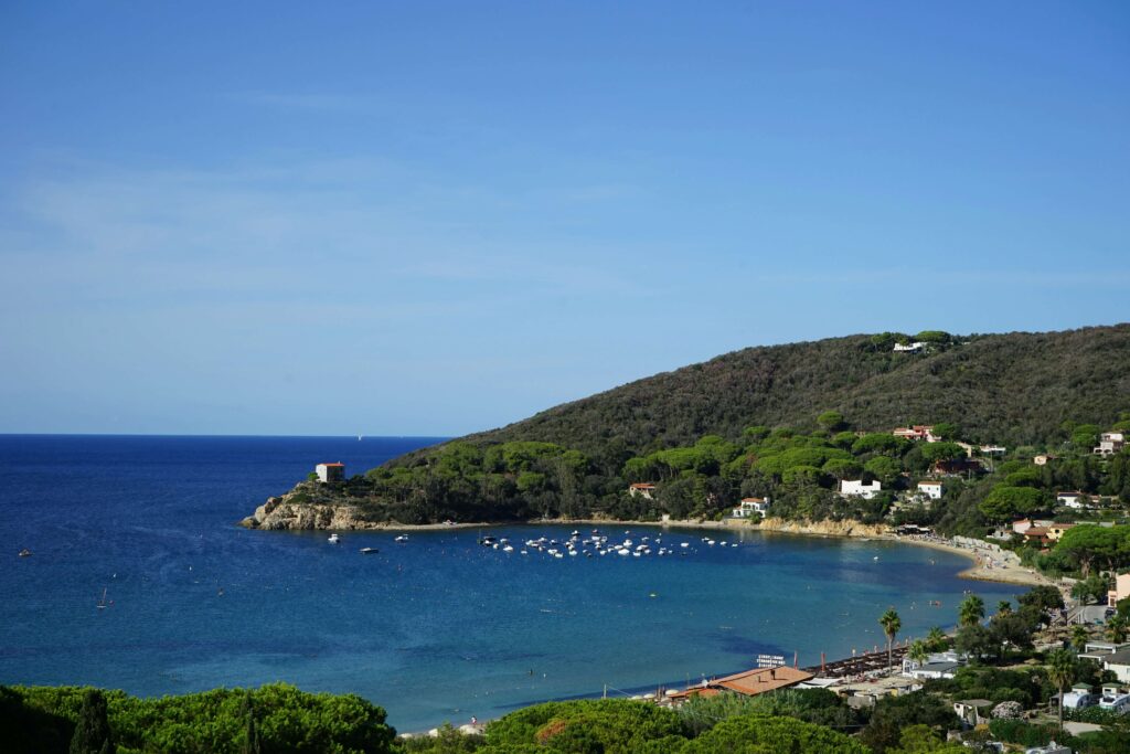 Vasta spiaggia di sabbia finissima a Procchio, Isola d'Elba, con acque cristalline e barche ancorate, ideale per una sosta in catamarano.